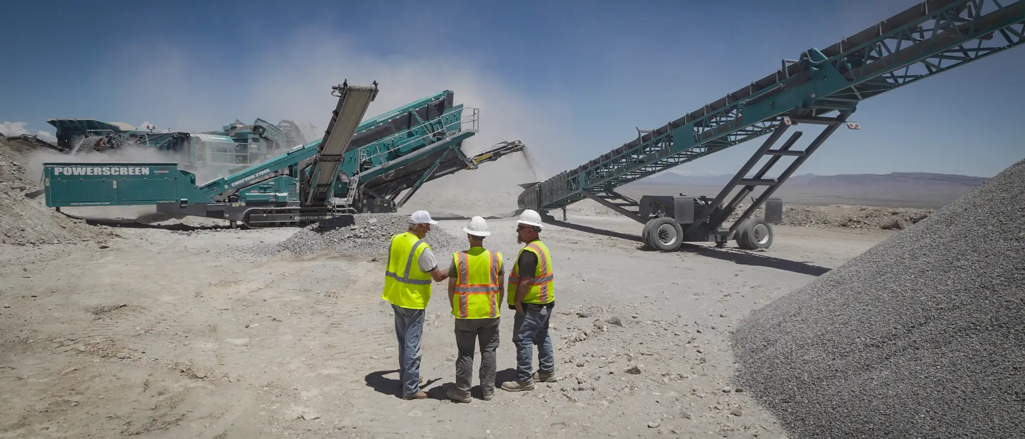 Three workers in high-visibility vests and hard hats standing before a screening plant and stacker conveyor