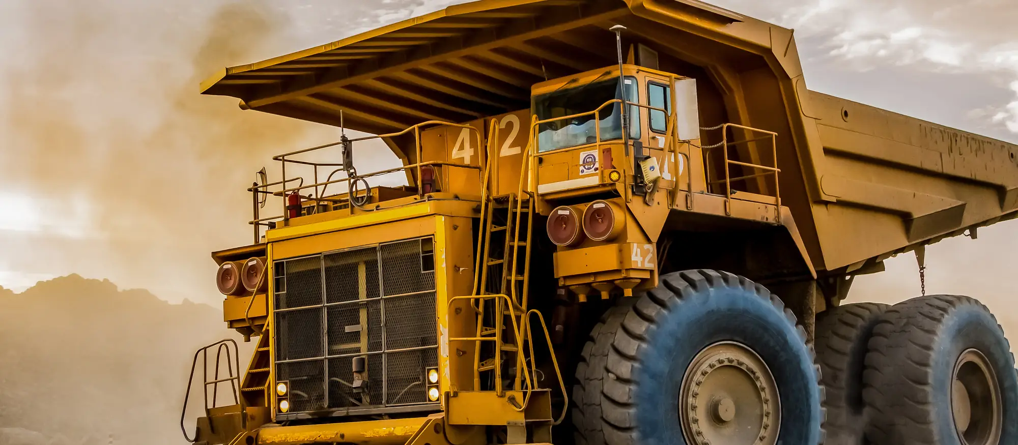 A loaded haul truck working through dust at a mine site at golden hour