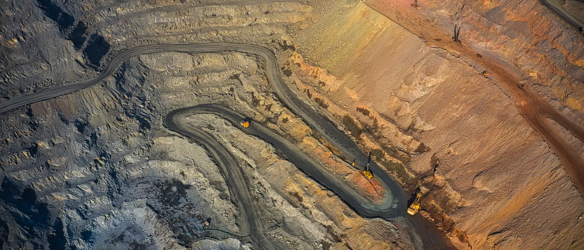 Aerial view of an open-pit mine's benches, haul roads switchbacking down through coloured ore