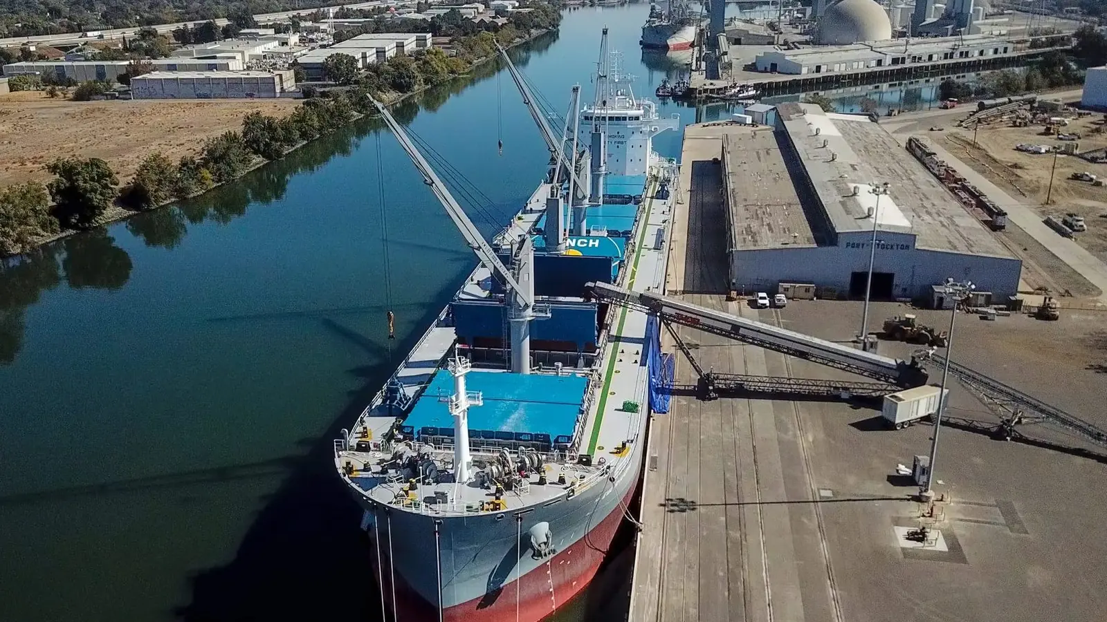A bulk carrier loading at a river port, conveyor boom swung over the hold